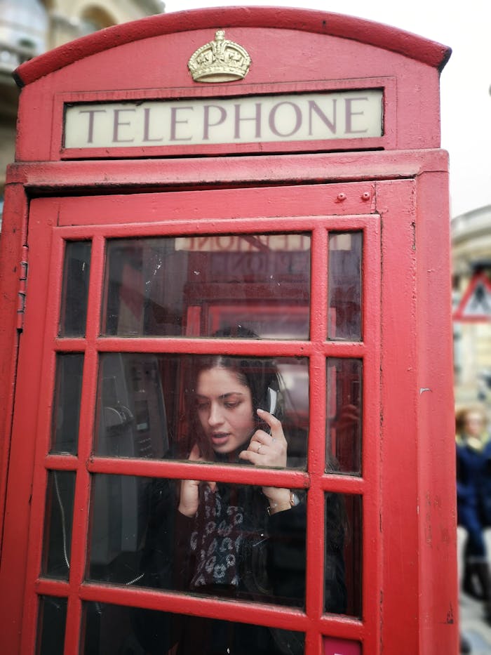 A woman using a vintage red telephone booth in London, capturing British nostalgia.