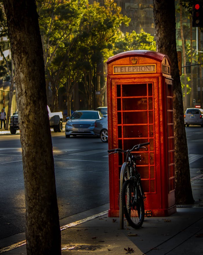 Vintage red telephone booth with bicycle in a vibrant urban setting at daytime.